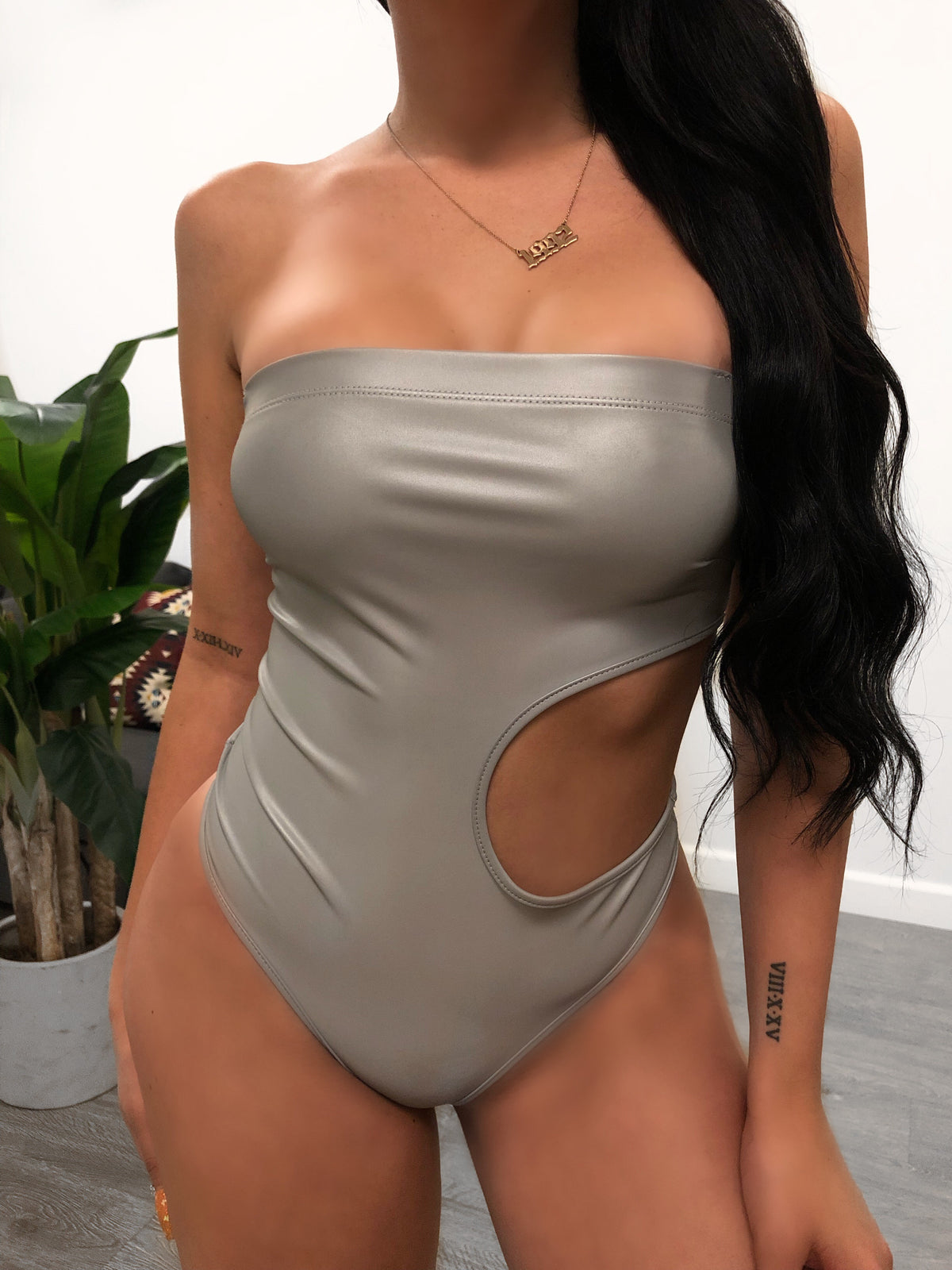 grey reflective strapless and sleeveless bodysuit, has oval shape opening on left ribs